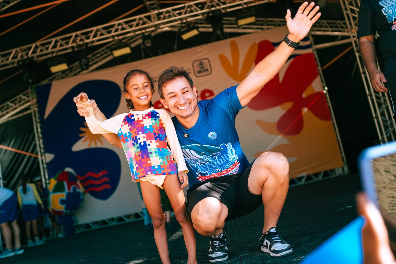 Criança sorrindo e pulando de alegria ao lado de uma voluntária durante atividade do Time da Inclusão