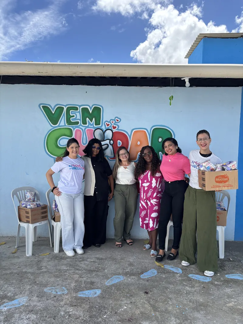 Seis voluntárias com caixas de alimentos doados, em frente ao mural “Vem Cuidar”